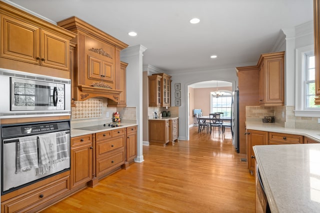 kitchen with light wood-type flooring, crown molding, stainless steel appliances, and tasteful backsplash