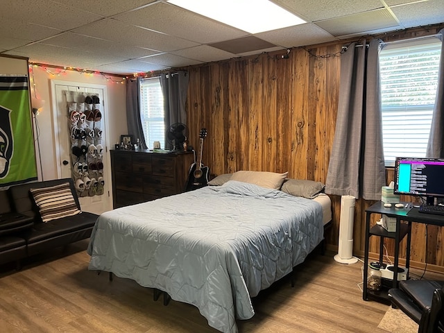 bedroom with light wood-type flooring, a paneled ceiling, and wooden walls