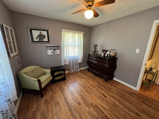 living area with ceiling fan, dark wood-type flooring, and a textured ceiling