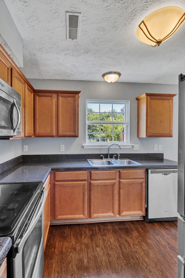 kitchen with sink, a textured ceiling, appliances with stainless steel finishes, and dark wood-type flooring