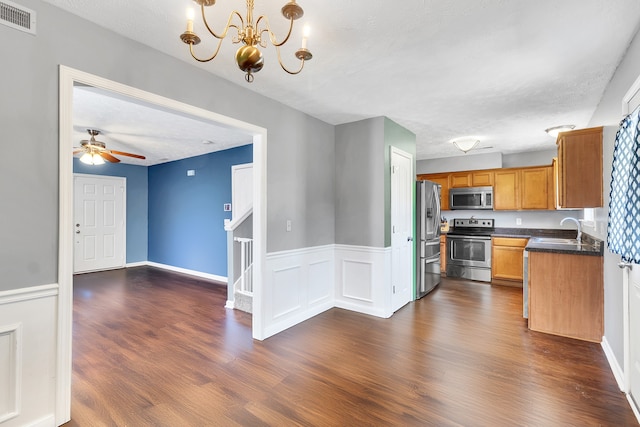 kitchen with appliances with stainless steel finishes, sink, ceiling fan with notable chandelier, dark wood-type flooring, and hanging light fixtures