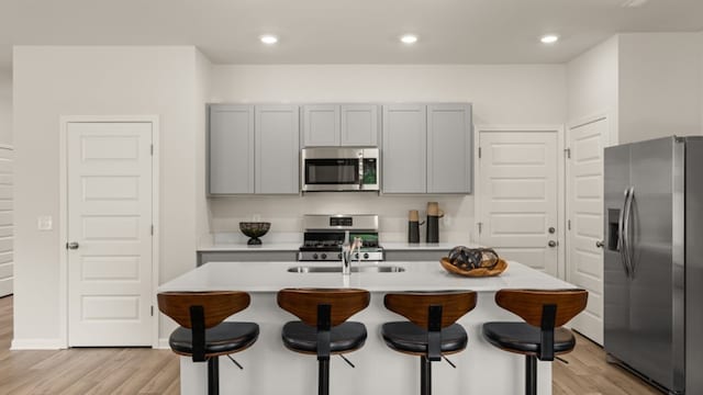 kitchen featuring stainless steel appliances, light hardwood / wood-style floors, a breakfast bar, and a kitchen island with sink