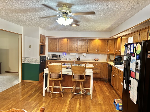 kitchen featuring black appliances, a kitchen island, ceiling fan, a breakfast bar, and light carpet