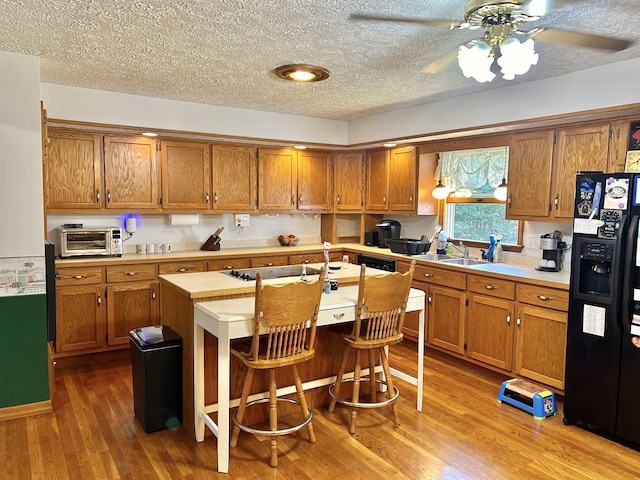 kitchen featuring hardwood / wood-style flooring, a breakfast bar, black fridge with ice dispenser, and ceiling fan