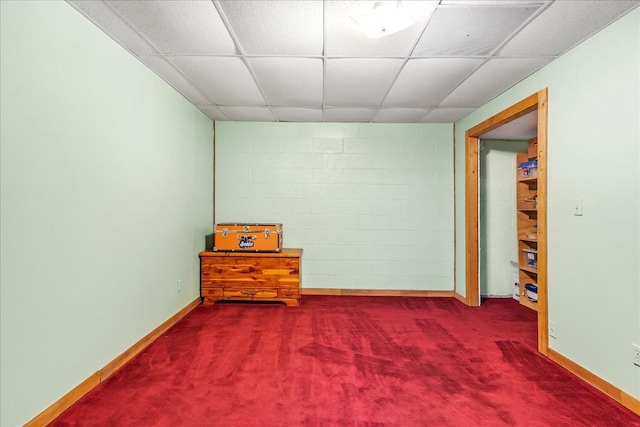 carpeted empty room with a drop ceiling, concrete block wall, and baseboards