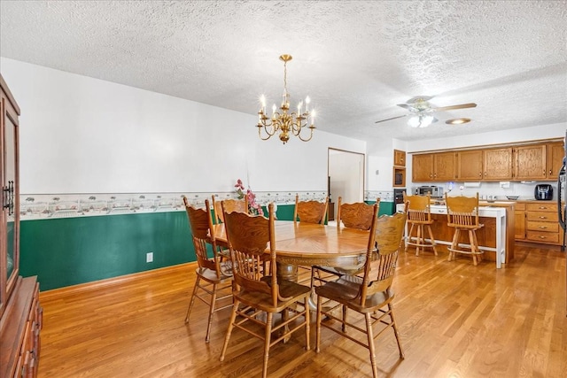 dining space featuring ceiling fan with notable chandelier, light wood-style flooring, a textured ceiling, and baseboards