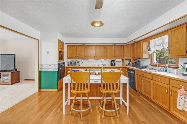 kitchen with light wood finished floors, light countertops, brown cabinets, black appliances, and a sink