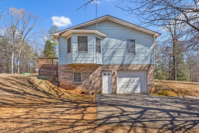 view of front of property featuring a garage, brick siding, a wooden deck, and aphalt driveway