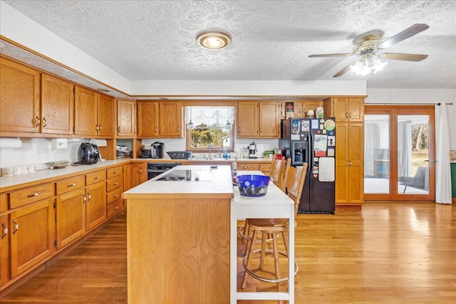 kitchen with light wood finished floors, light countertops, a kitchen breakfast bar, brown cabinetry, and black fridge with ice dispenser