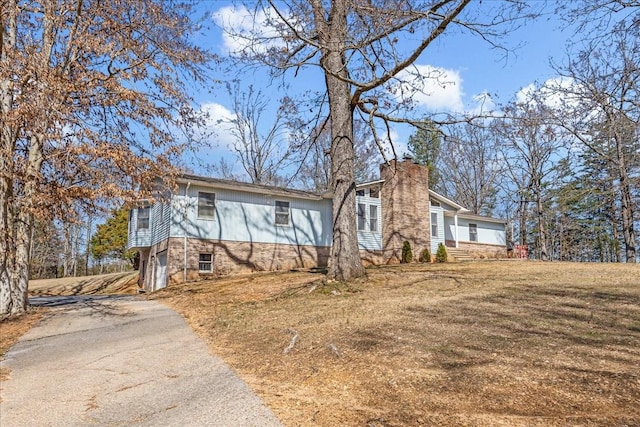 view of front of home with driveway, a chimney, and a front yard