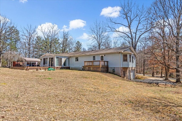 back of house with a lawn, an attached garage, a wooden deck, and a sunroom