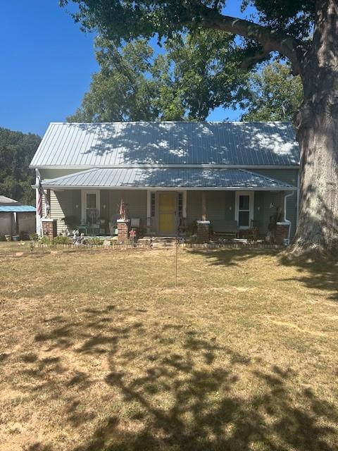 rear view of property featuring metal roof, covered porch, and a lawn