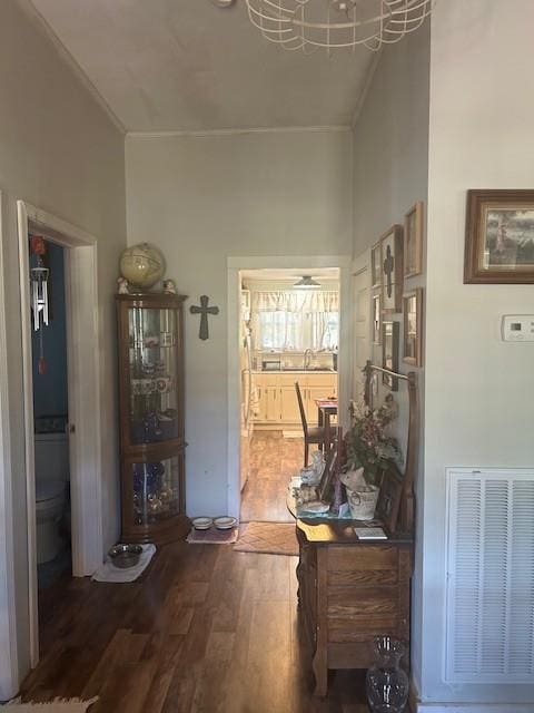 hallway featuring ornamental molding, visible vents, and wood finished floors