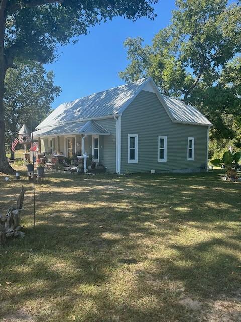 view of side of home featuring metal roof, covered porch, and a lawn