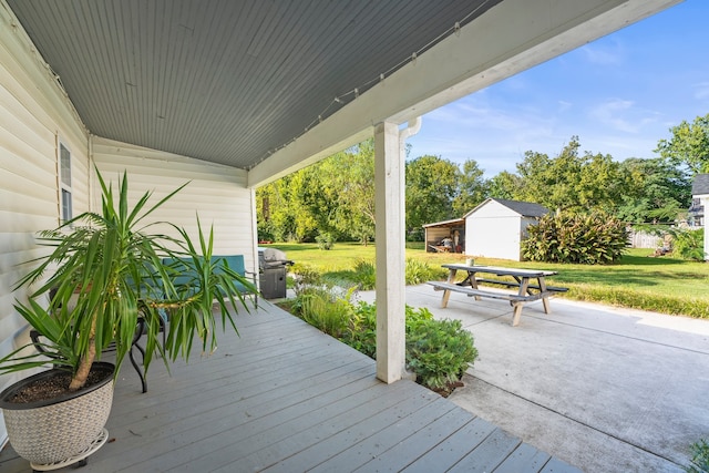 deck with a storage shed, a patio area, a lawn, and a grill