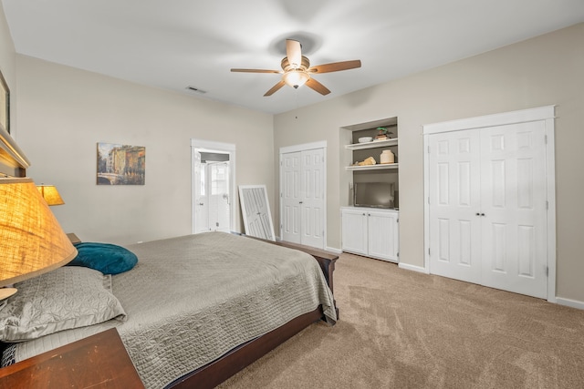 bedroom featuring ceiling fan, light carpet, and multiple closets