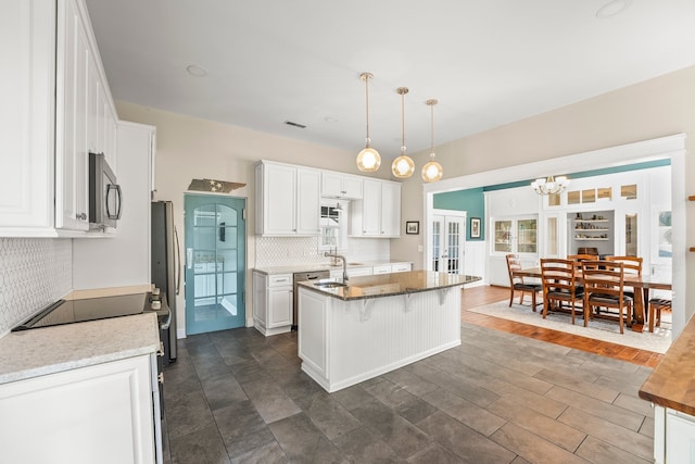 kitchen featuring a kitchen island with sink, tasteful backsplash, stainless steel appliances, hanging light fixtures, and dark hardwood / wood-style floors