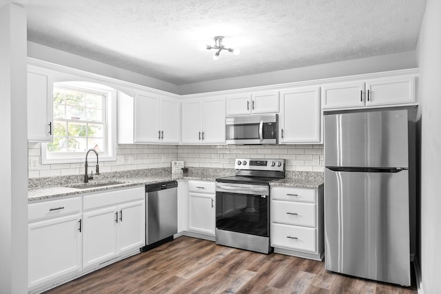 kitchen featuring white cabinets, appliances with stainless steel finishes, light stone counters, sink, and dark hardwood / wood-style floors