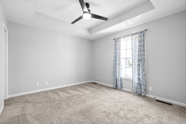 empty room with a tray ceiling, ceiling fan, and light carpet