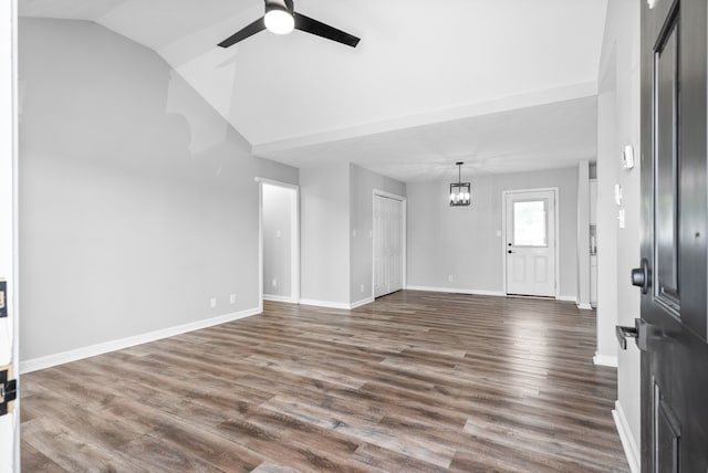 unfurnished living room with ceiling fan with notable chandelier, dark hardwood / wood-style flooring, and vaulted ceiling