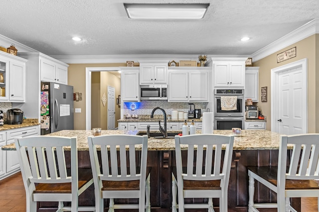 kitchen featuring crown molding, white cabinetry, decorative backsplash, appliances with stainless steel finishes, and a center island with sink