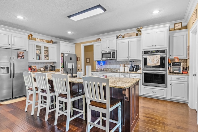 kitchen featuring crown molding, dark hardwood / wood-style floors, appliances with stainless steel finishes, and a kitchen island with sink