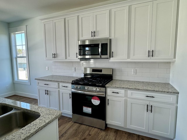 kitchen featuring decorative backsplash, light stone countertops, stainless steel appliances, dark wood-type flooring, and white cabinetry