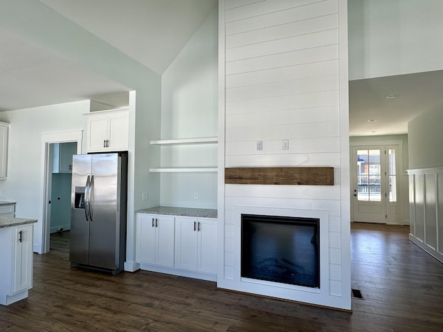 kitchen featuring dark wood-type flooring, vaulted ceiling, stainless steel fridge, light stone countertops, and white cabinetry