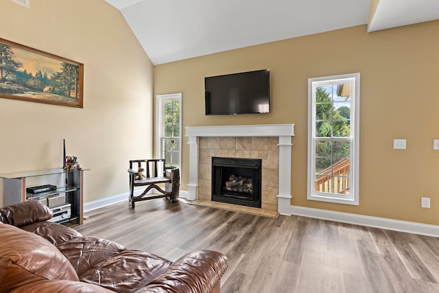 living room featuring wood-type flooring, vaulted ceiling, a tile fireplace, and plenty of natural light