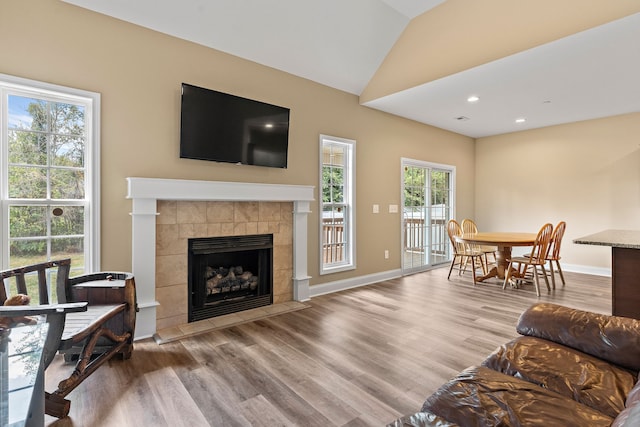 living room with light wood-type flooring, a tiled fireplace, vaulted ceiling, and plenty of natural light