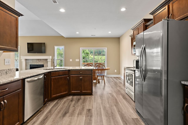 kitchen featuring appliances with stainless steel finishes, a fireplace, light stone countertops, light hardwood / wood-style flooring, and sink