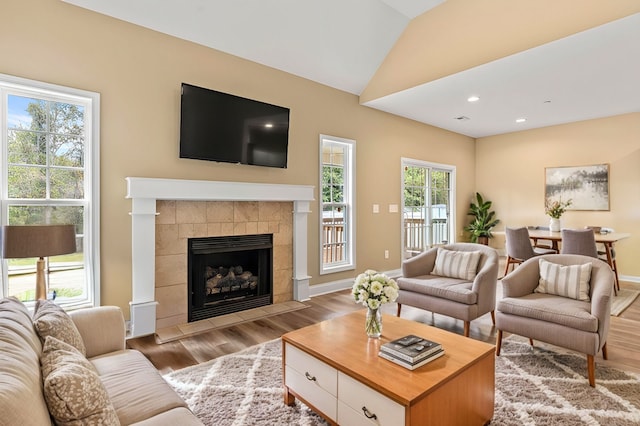 living room featuring light wood-type flooring, a tiled fireplace, lofted ceiling, and a wealth of natural light