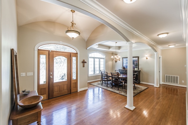 entrance foyer featuring crown molding, wood-type flooring, an inviting chandelier, and decorative columns