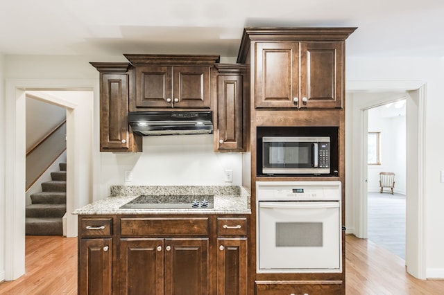 kitchen with light hardwood / wood-style flooring, dark brown cabinets, black electric cooktop, and white oven