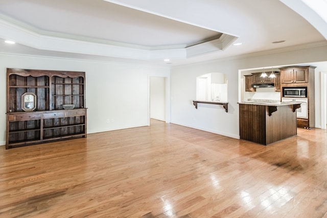 kitchen featuring crown molding, a kitchen breakfast bar, built in microwave, a raised ceiling, and light hardwood / wood-style floors