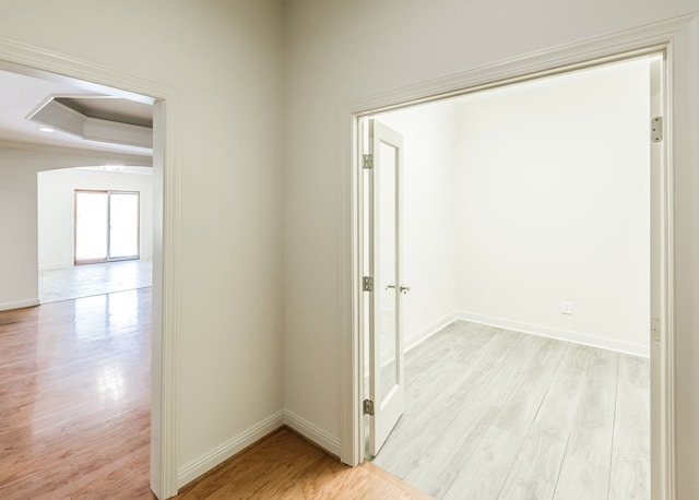 hall with crown molding, light hardwood / wood-style flooring, and a tray ceiling