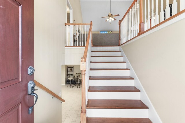 stairway featuring a high ceiling, tile patterned flooring, and ceiling fan