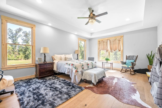 bedroom with light wood-type flooring, a tray ceiling, ceiling fan, and recessed lighting