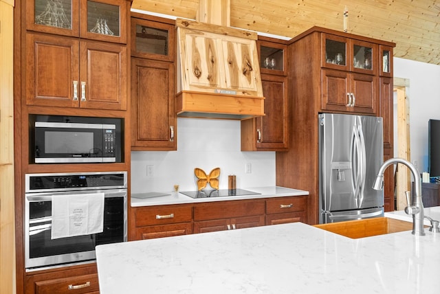 kitchen featuring stainless steel appliances, custom exhaust hood, glass insert cabinets, and light stone countertops