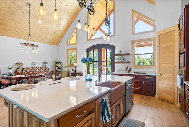 kitchen with an island with sink, light wood finished floors, hanging light fixtures, and french doors