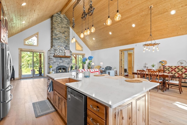 kitchen featuring stainless steel appliances, hanging light fixtures, open floor plan, a kitchen island with sink, and a stone fireplace