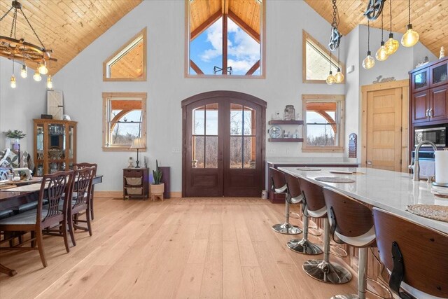 foyer entrance featuring arched walkways, wooden ceiling, french doors, light wood-type flooring, and high vaulted ceiling