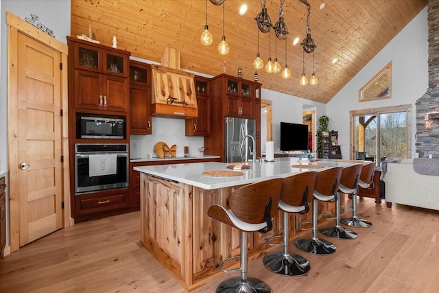 kitchen featuring open floor plan, a kitchen island with sink, stainless steel appliances, light countertops, and pendant lighting