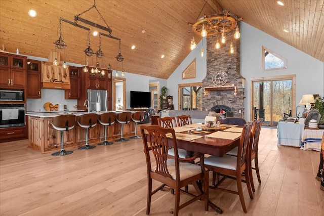 dining room with high vaulted ceiling, wood ceiling, a stone fireplace, and light wood finished floors