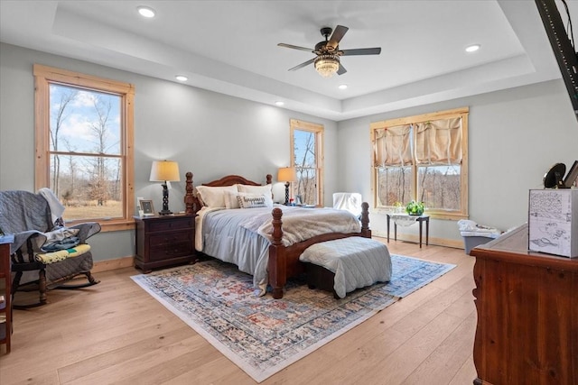 bedroom with recessed lighting, light wood-type flooring, a raised ceiling, and baseboards