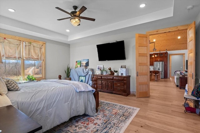 bedroom featuring light wood-style flooring, a raised ceiling, freestanding refrigerator, and recessed lighting