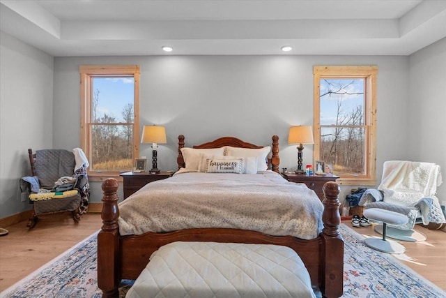 bedroom featuring a raised ceiling, multiple windows, baseboards, and wood finished floors