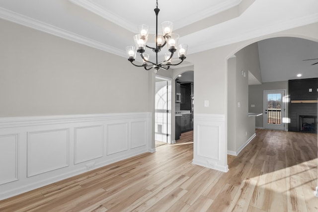 unfurnished dining area featuring a tray ceiling, a fireplace, arched walkways, and light wood finished floors