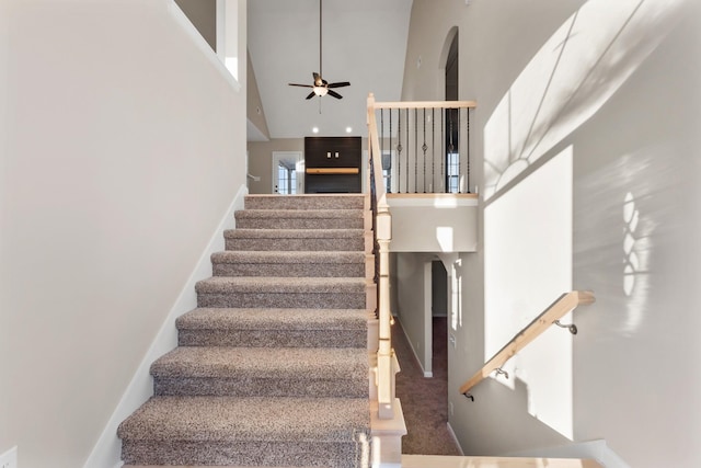 stairway with a ceiling fan, a towering ceiling, and baseboards