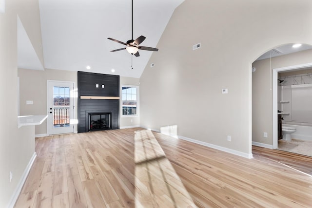 unfurnished living room featuring arched walkways, ceiling fan, a fireplace, baseboards, and light wood-style floors